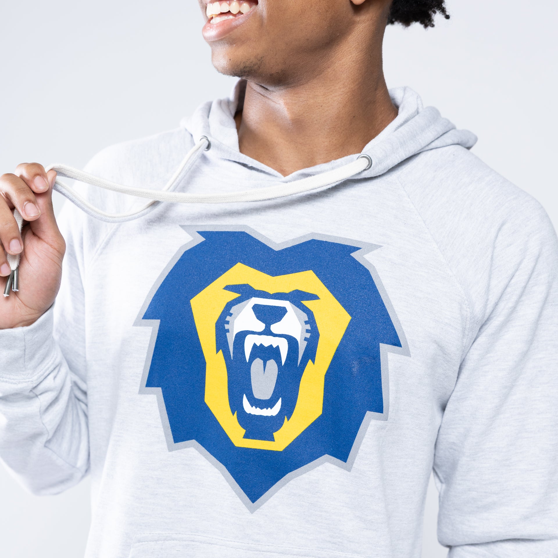 A man wearing a light heather gray hoodie with a large blue and yellow roaring lion graphic on the chest, shown against a light gray studio background.