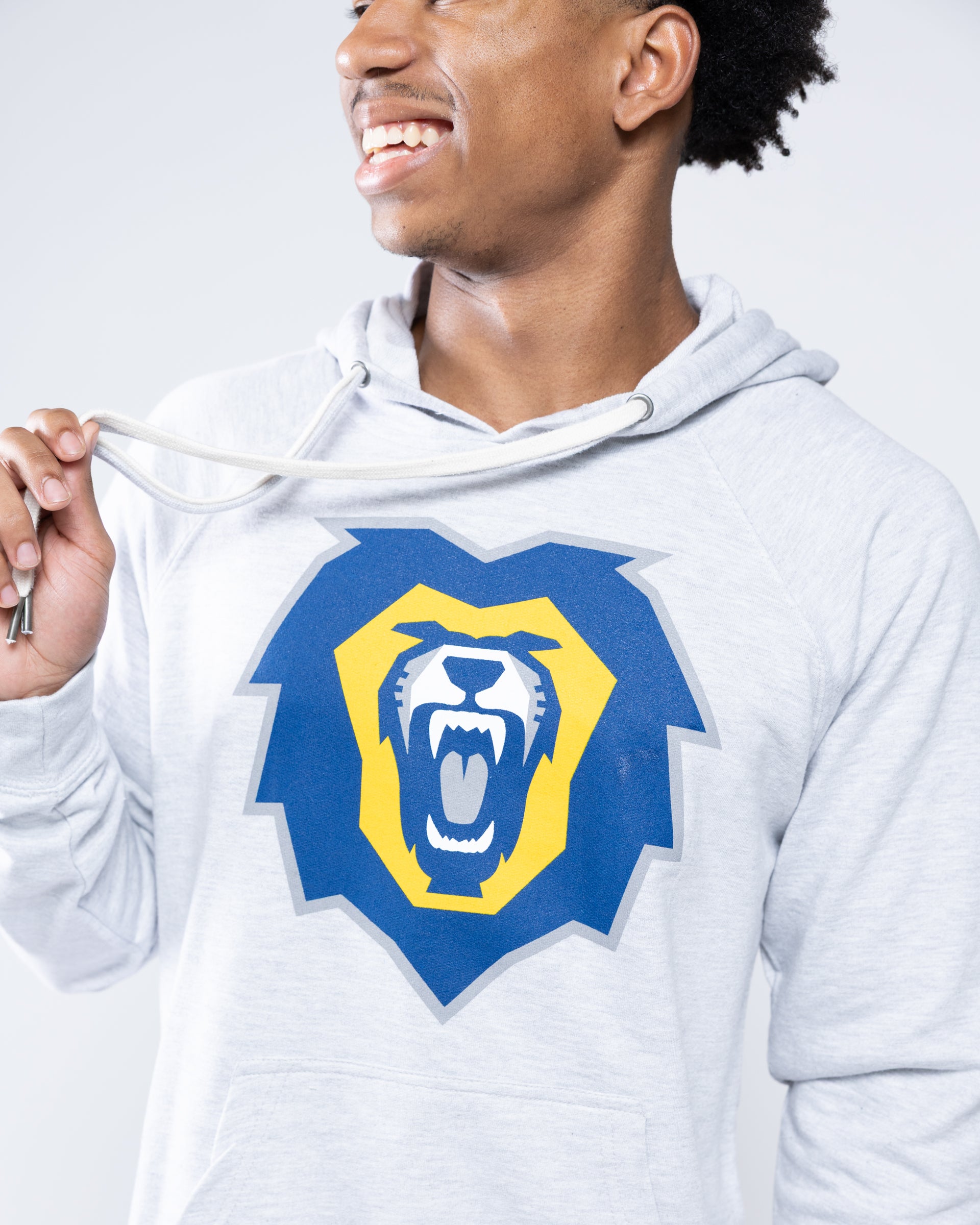 A man wearing a light heather gray hoodie with a large blue and yellow roaring lion graphic on the chest, shown against a light gray studio background.